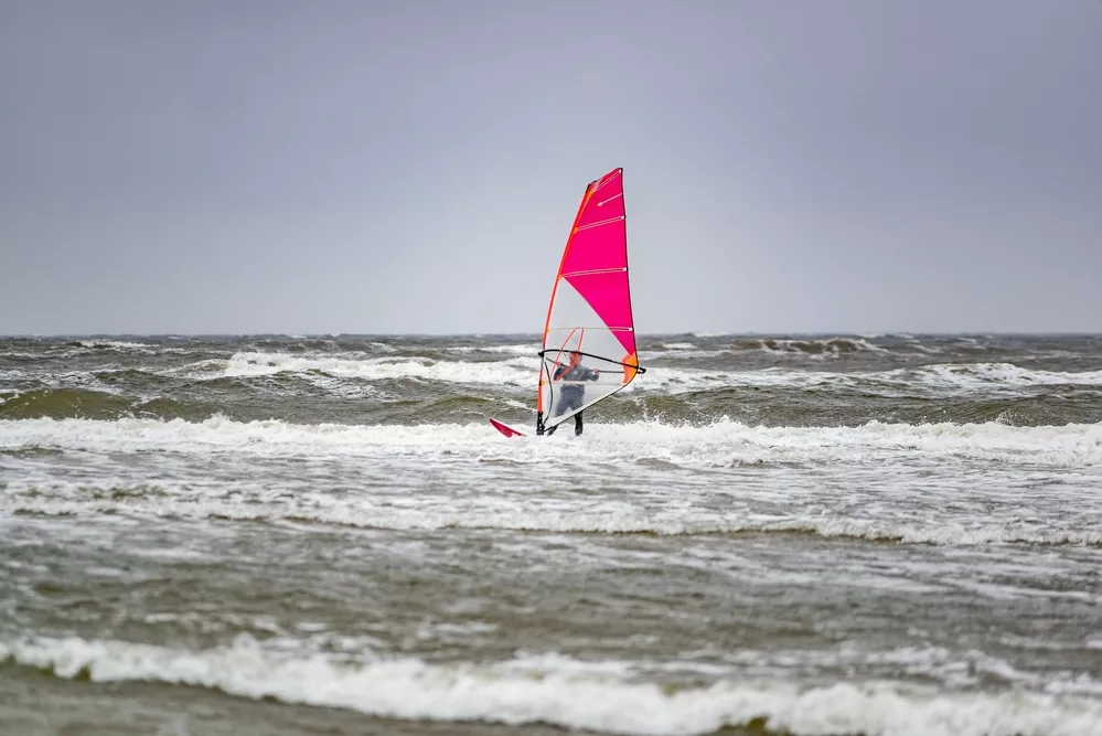 surfer met rode surfplank tussen de golven op donkere dag