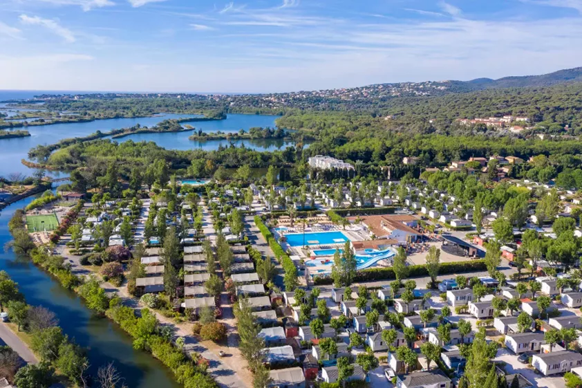 vakantiehuisjes in nette rijen met zwemad en rivier tussen de bomen. Camping Sandaya Riviera d'azur