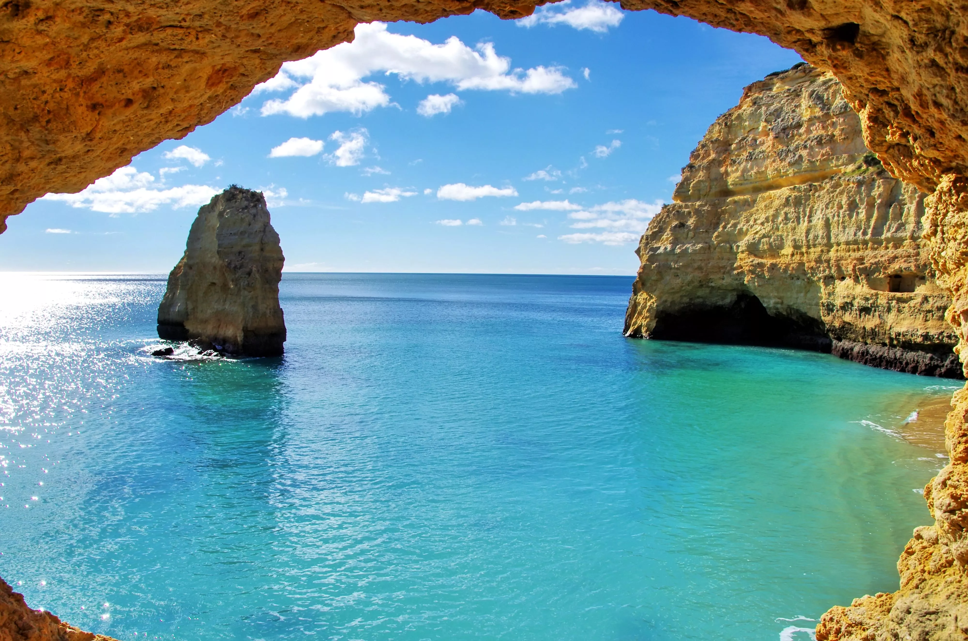 Blik op turquoise zee en hoge rotsformaties aan de Algarve-kust, gezien vanuit een natuurlijke grotopening.