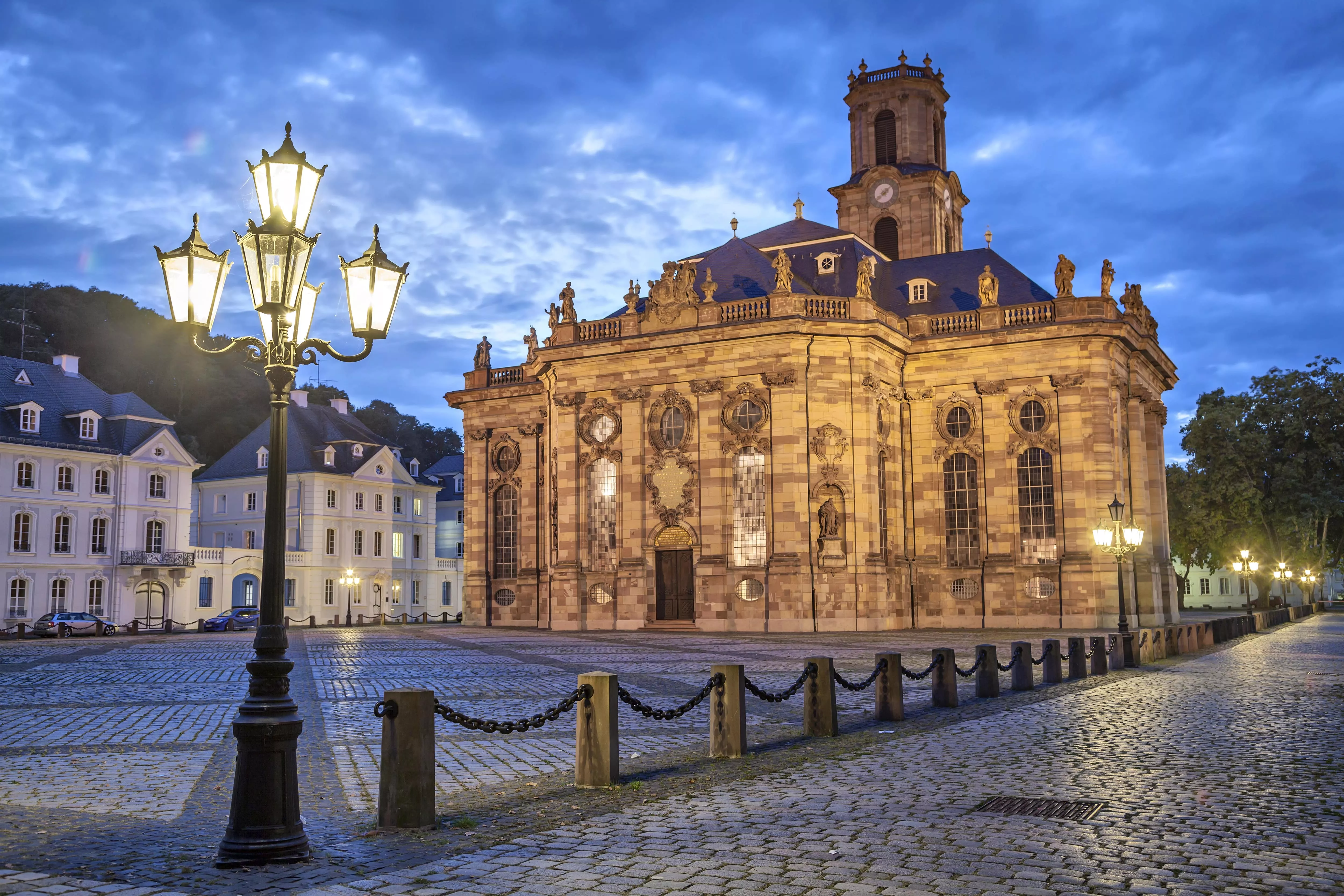De Ludwigskirche in Saarbrücken straalt sfeervol op een leeg plein bij avondlicht.